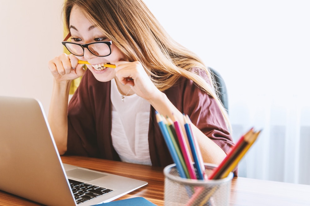 frustrated woman biting a pencil looking at laptop computer