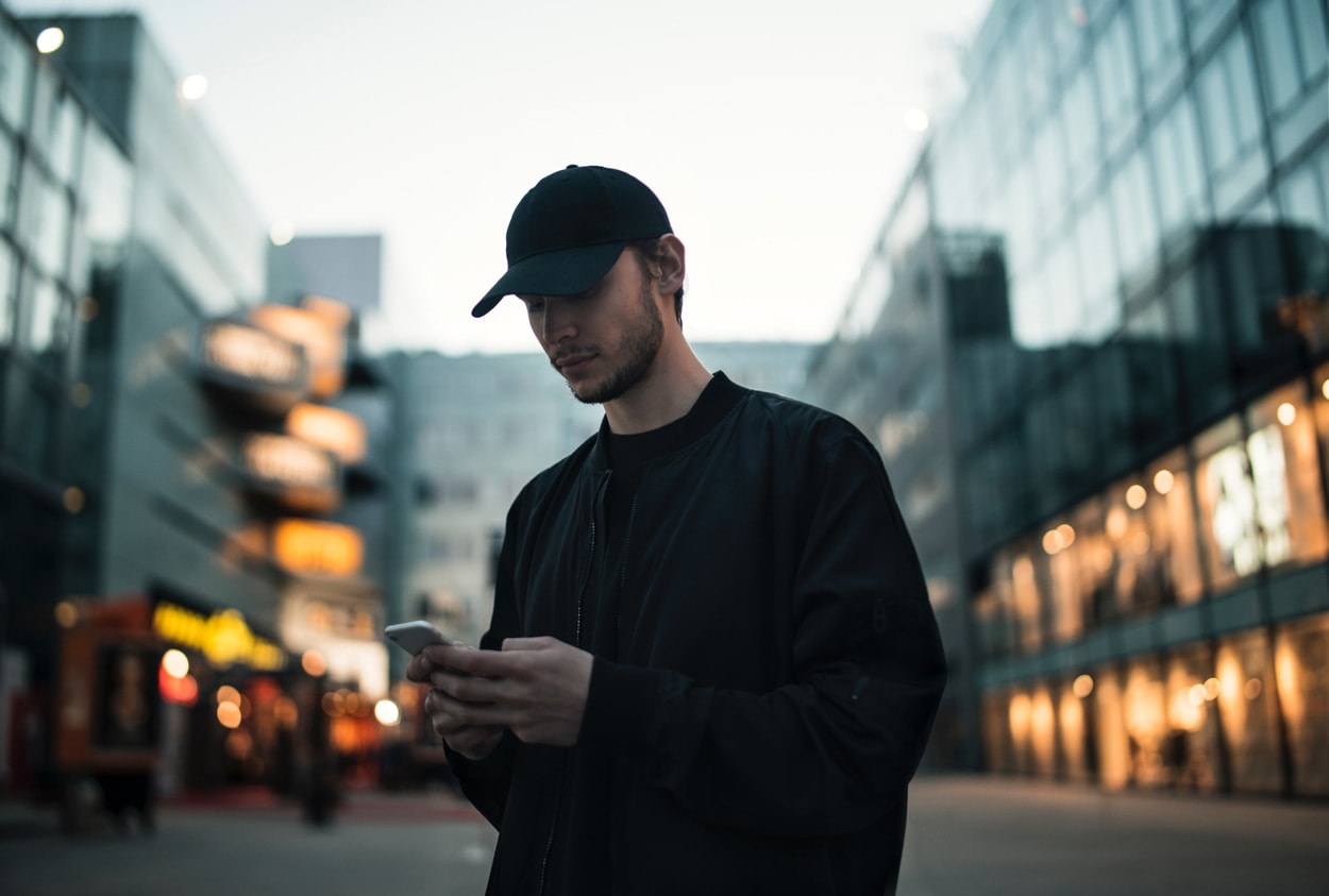 man walking in black jacket and black hat using mobile phone